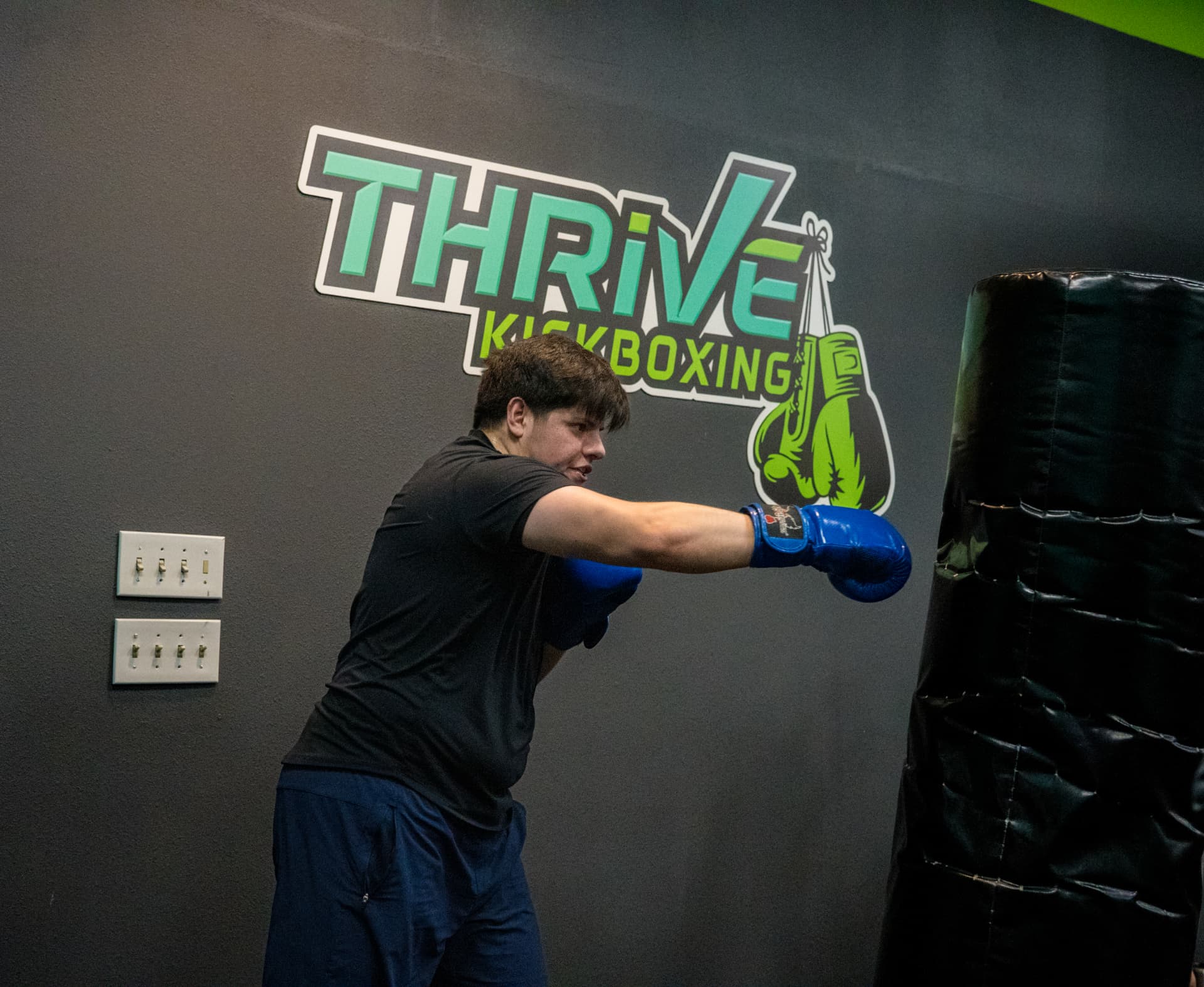 Male member throwing a jab on the bag under the Thrive Kickboxing logo