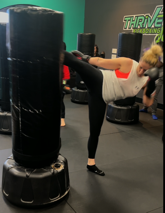 Member landing a high kick on a heavy bag during a Thrive class